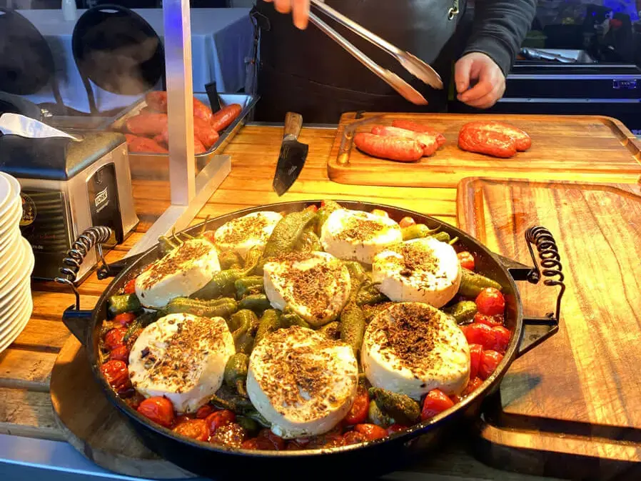 Grillweltmeister Marco Greulich bereitet gegrilltes Gemüse, Salciccia-Wurst und Käse unter Wärmelampen zu.