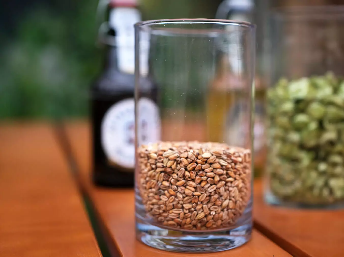 Ein Glas mit hellem Malz auf einem Holztisch, im Hintergrund eine Flensburger Bierflasche verschwommen.