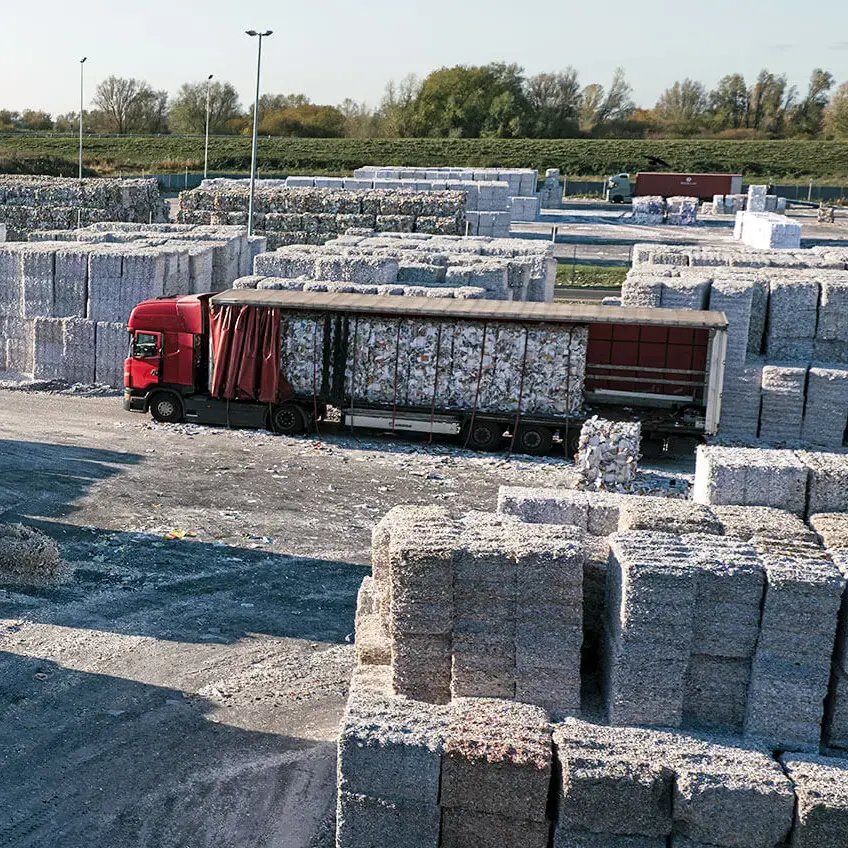 Altpapier-Recyclinghof mit gestapelten Papierballen und rotem LKW bei Steinbeis.