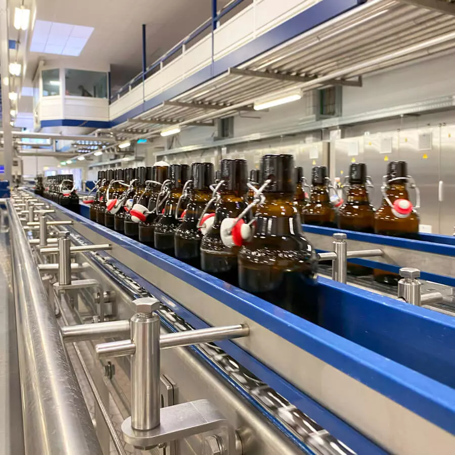 Flensburger Pilsener läuft eine kurze Strecke geöffnet, aber schon befüllt, auf dem Band, bevor der Bügelverschluss geschlossen wird.