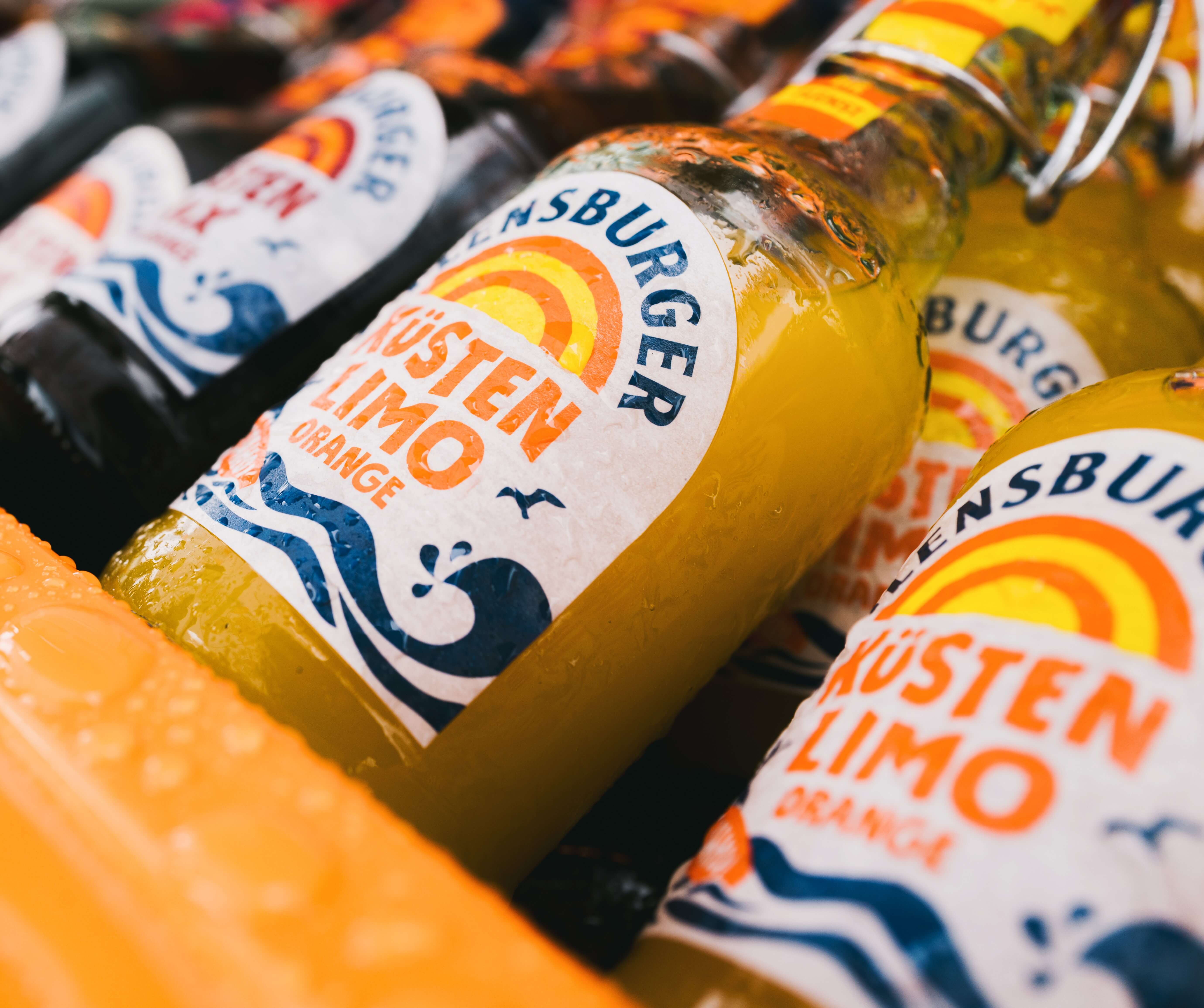 Flensburger Küstenlimo "Orange" in einer Bügelverschlussflasche mit fruchtiger Orangenfarbe und einem Wassertropfen-bedeckten Etikett, das den Fruchtsaftgehalt von 10 % hervorhebt.