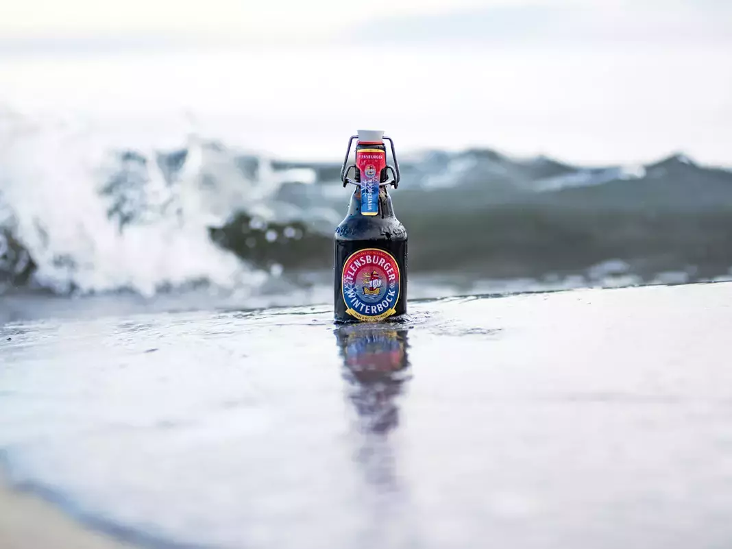 Eine Flasche Flensburger Winterbock steht in der Brandung am Meer in der Welle.